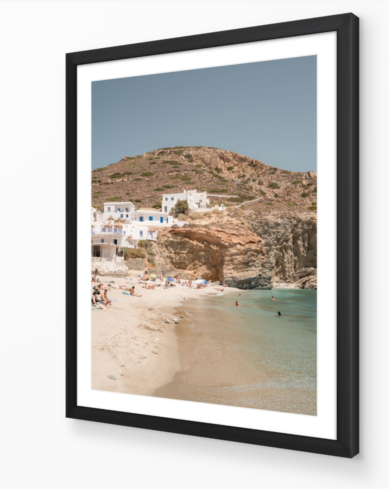Agali Beach – Folegandros fine-art print in black frame by Sam Smeaton — warm Cycladic coastal scene with cliffs, clear sea, and white village architecture