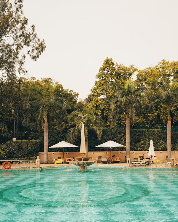Luxury resort pool surrounded by palm trees and white umbrellas under a soft sky