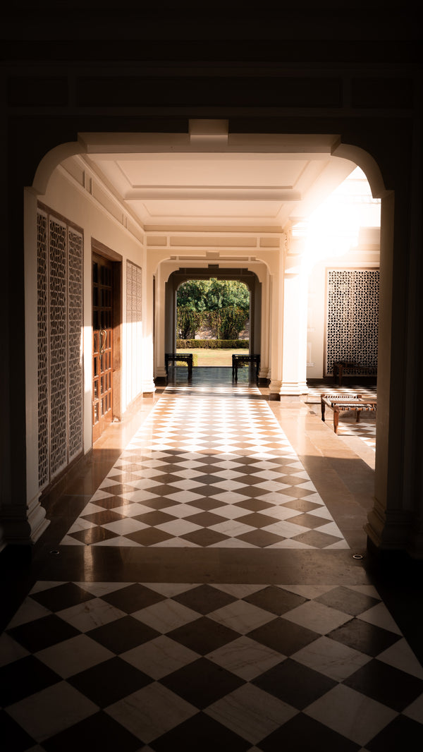 Elegant arched hotel corridor with black and white checkered marble floor and garden view.