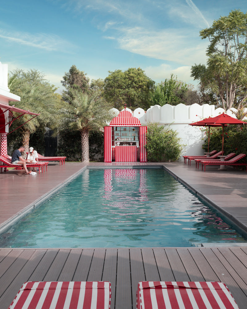 Poolside pavilion with red umbrellas and palm trees at Villa Palladio Jaipur — luxury hospitality photography by Sam Smeaton.
