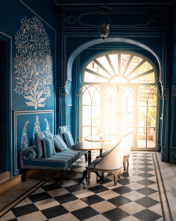 Elegant blue hotel lounge with arched doorway, tree mural, and natural light streaming in.