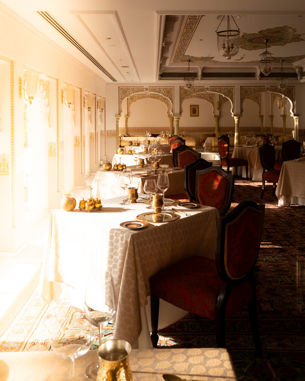Elegant hotel dining room with white table linens, gold accents, and traditional Indian décor.