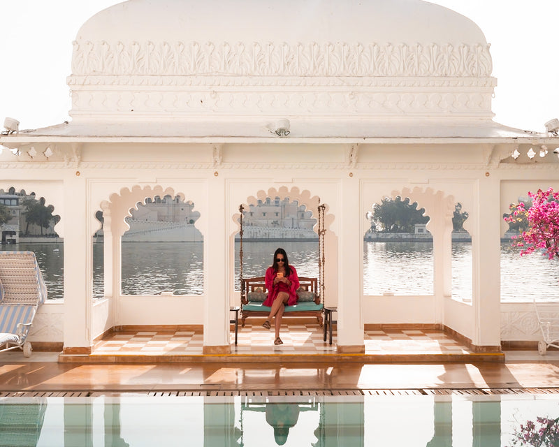 Guest seated on traditional swing overlooking Lake Pichola at Taj Lake Palace Udaipur, surrounded by white marble arches and blooming bougainvillea.