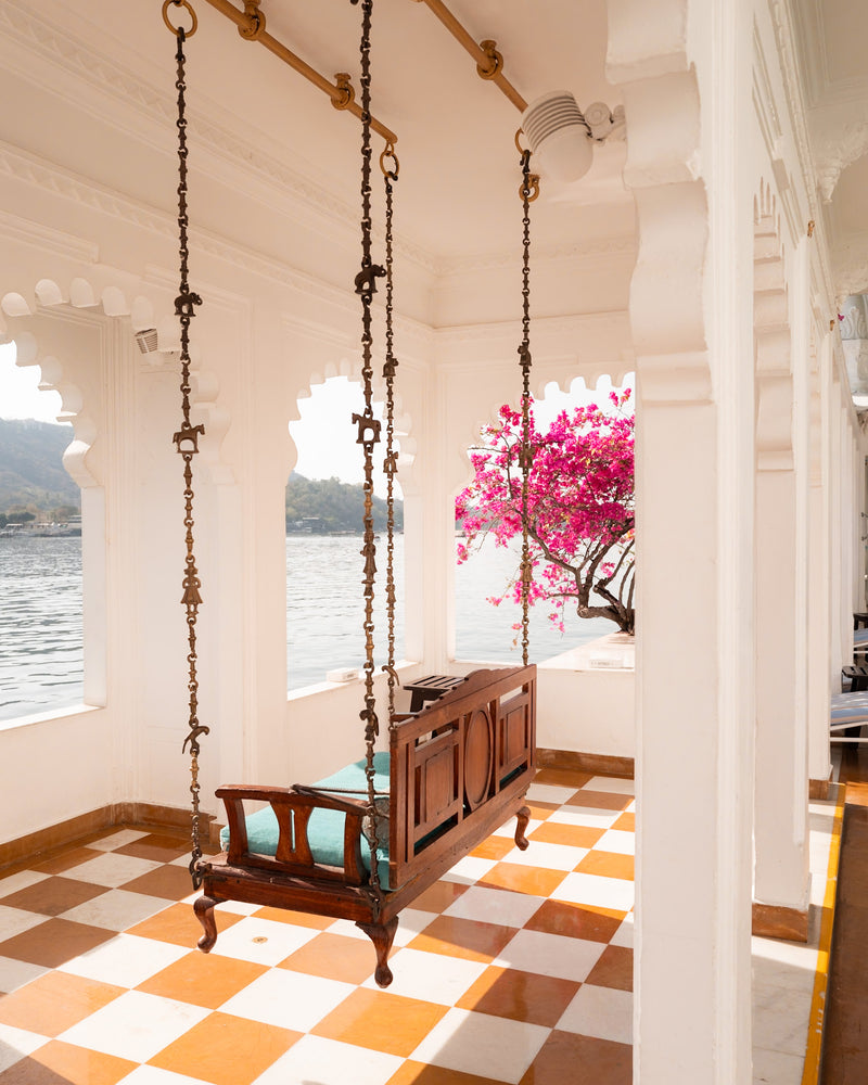 Wooden swing seat hanging between white marble arches with pink bougainvillea overlooking Lake Pichola at Taj Lake Palace Udaipur — photographed by Sam Smeaton.