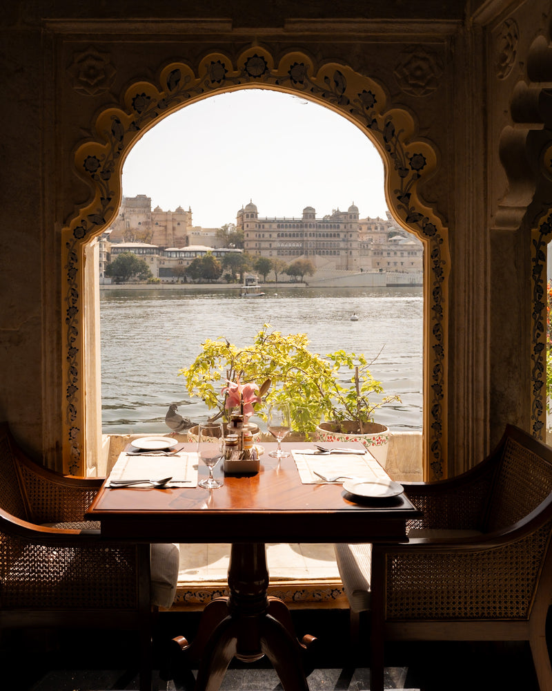 Lake-view dining table framed by an arched window at Taj Lake Palace Udaipur, overlooking City Palace — boutique hotel photography by Sam Smeaton.