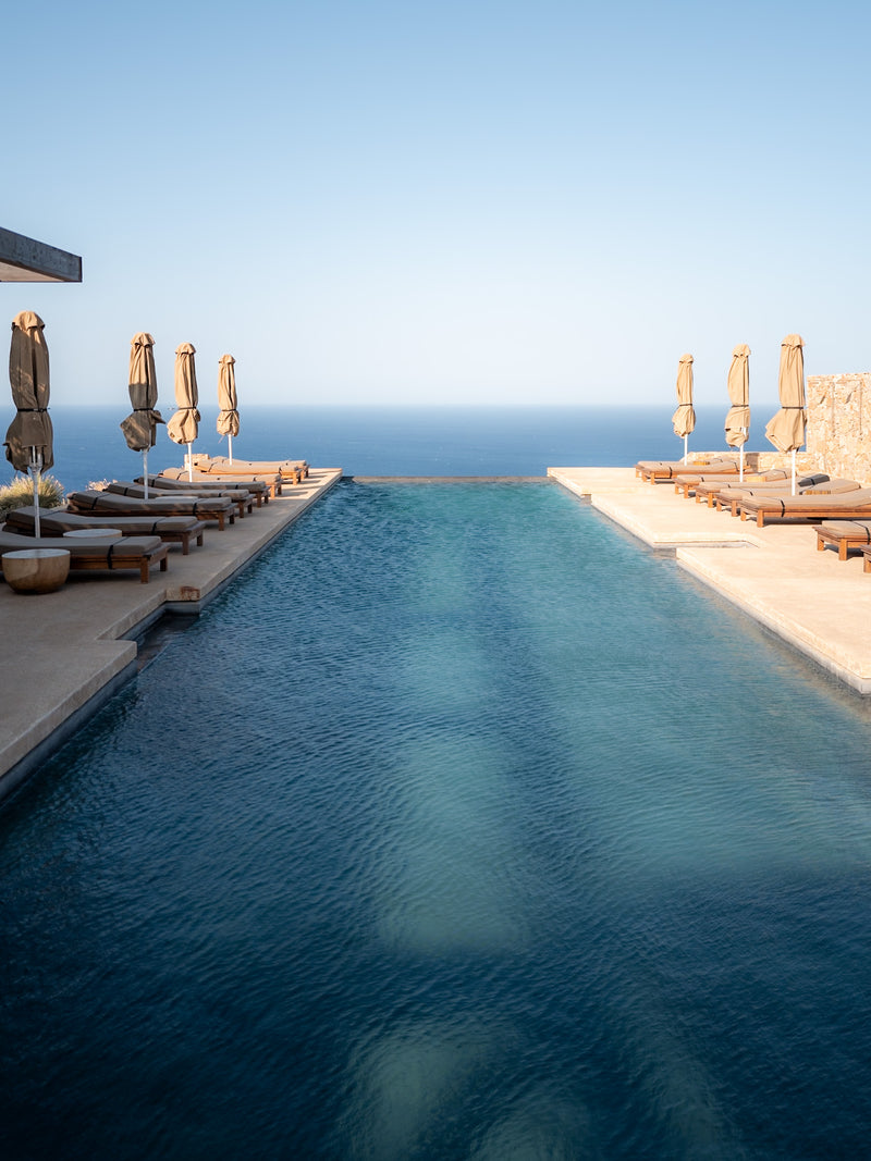 Infinity-edge pool and umbrellas facing open sea, photographed in soft morning light.