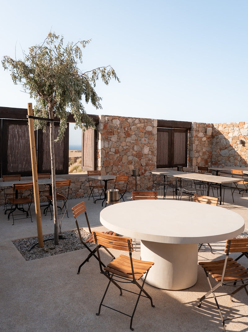 Outdoor dining courtyard with round stone table and timber chairs in soft sunlight.