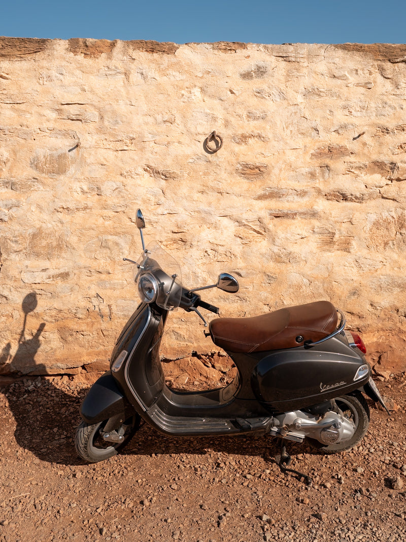 Vintage Vespa against rustic stone wall, editorial travel photography in Greece.