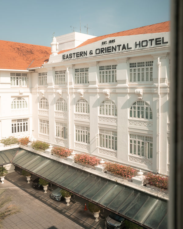 Historic white colonial façade of the Eastern & Oriental Hotel with striped awnings and arched windows.
