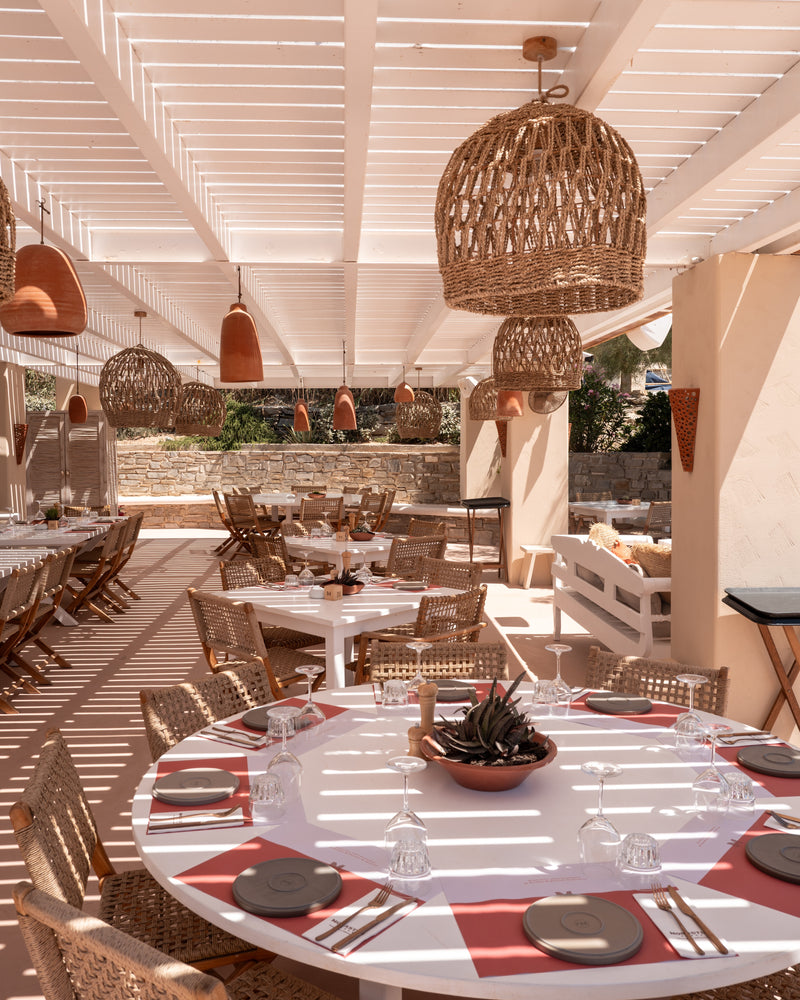 Editorial restaurant scene with rattan pendants and long tables in natural light.