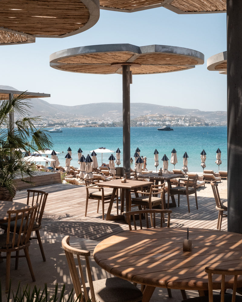 Luxury beachside restaurant with straw umbrellas and turquoise sea backdrop.