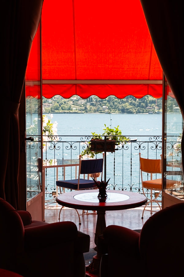 Romantic balcony overlooking lake with red canopy, wrought iron railing, and cafe table.
