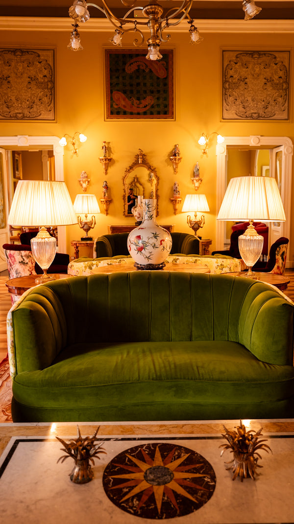 Vintage-inspired hotel lounge with green velvet sofa, ornate lamps, and gilded mirrors.