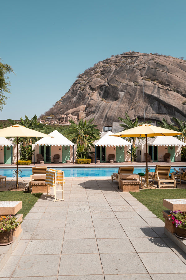 Luxury desert resort with mountain backdrop, white cabanas, and turquoise pool.