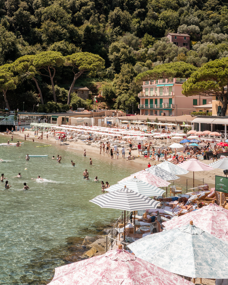 Fine-art photography print of Paraggi Beach by Sam Smeaton — striped parasols, turquoise water, and Portofino’s cove, captured on the Italian Riviera and printed on archival matte fine-art paper, 50×75 cm.