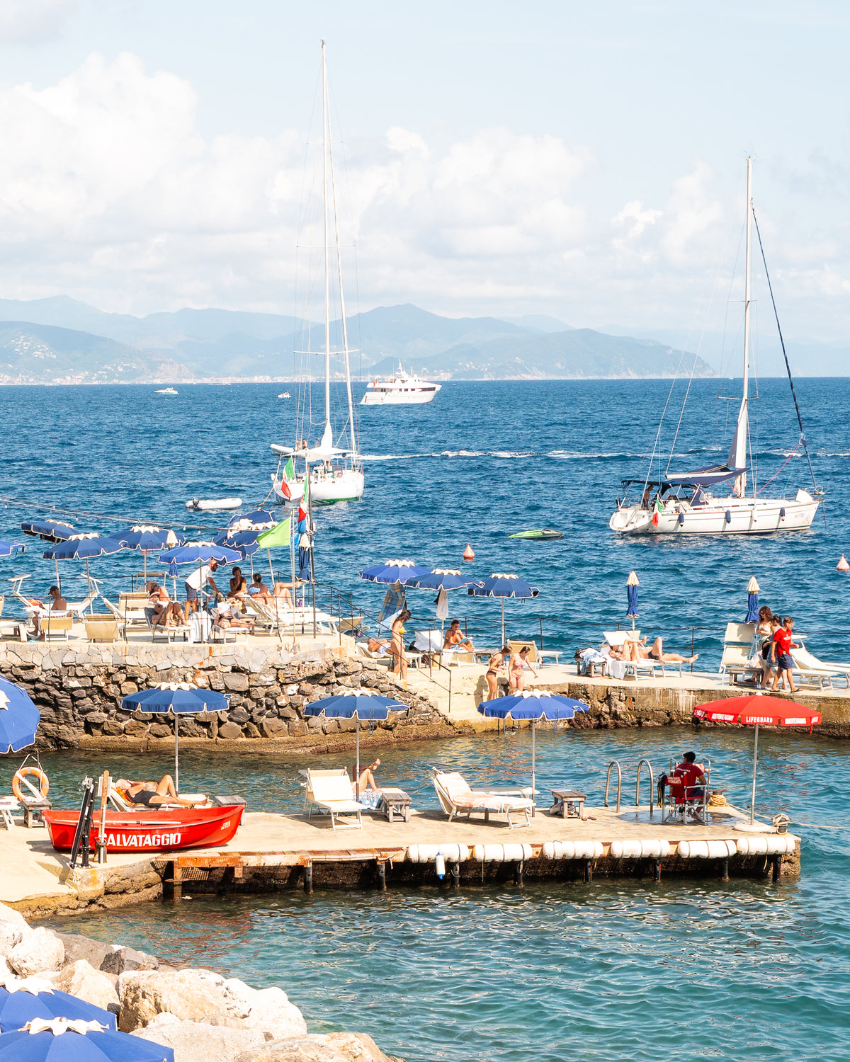 Fine-art photography print of Santa Margherita by Sam Smeaton — cobalt-blue umbrellas, turquoise Mediterranean water, and red lifeguard boat, Italian Riviera wall art printed on premium matte paper, 20×30 inches.