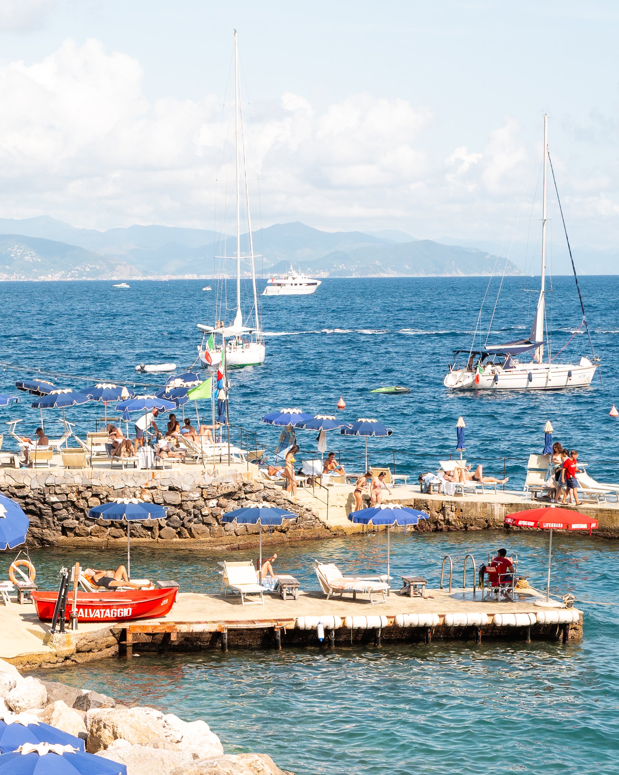 Fine-art photography print of Santa Margherita by Sam Smeaton — cobalt-blue umbrellas, turquoise Mediterranean water, and red lifeguard boat, Italian Riviera wall art printed on premium matte paper, 20×30 inches.